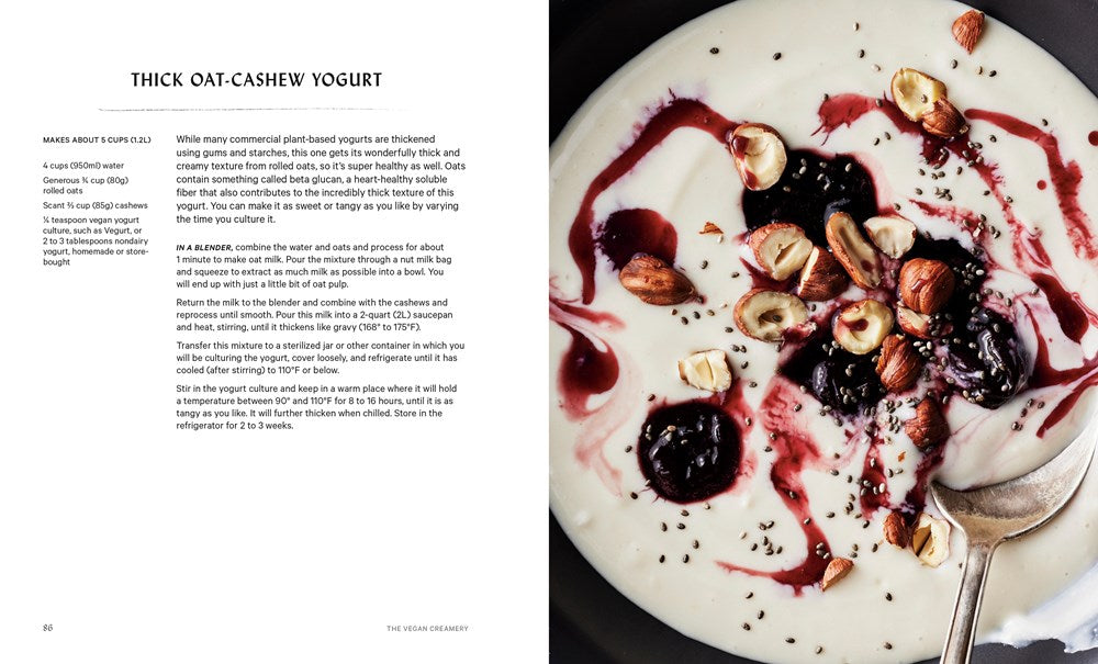 A bowl of thick, creamy white yogurt with berry sauce, hazelnuts, and chia seeds sits beside a recipe for oat-cashew yogurt inspired by Vegan Creamery by Miyoko Schinner (Signed & Personalized) from Yu & Me Books. A spoon rests in the bowl.